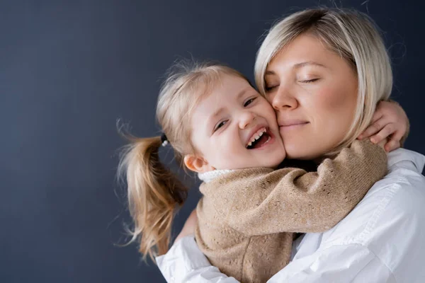 Lachendes Mädchen umarmt Mutter, während es isoliert auf schwarz in die Kamera schaut — Stockfoto
