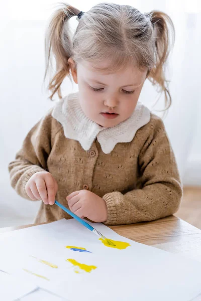 Kleines Mädchen mit Pferdeschwänzen Zeichnung mit blauen und gelben Farben zu Hause — Stockfoto