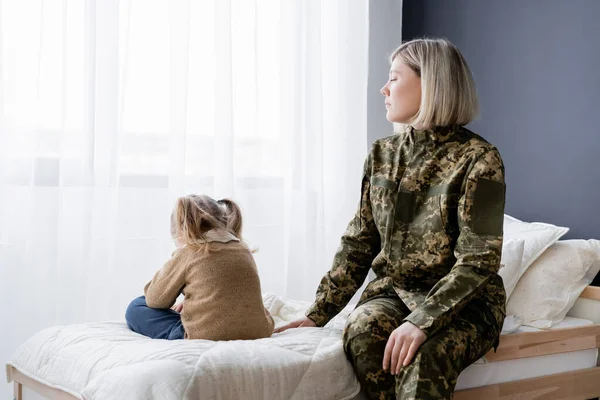 Frau in Militäruniform sitzt auf Bett neben beleidigter Tochter — Stockfoto