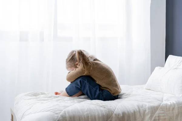Seitenansicht eines aufgebrachten Mädchens, das sein Gesicht verschleiert, während es zu Hause auf dem Bett sitzt — Stockfoto