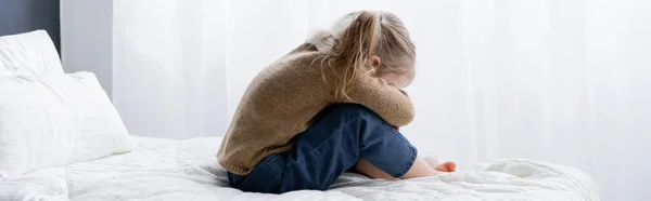 Seitenansicht des aufgebrachten Mädchens, das Gesicht verdeckt, während es auf dem Bett sitzt, Banner — Stockfoto