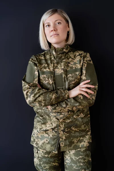 Bionda militare donna in piedi con le braccia incrociate e guardando la fotocamera isolata su nero — Foto stock