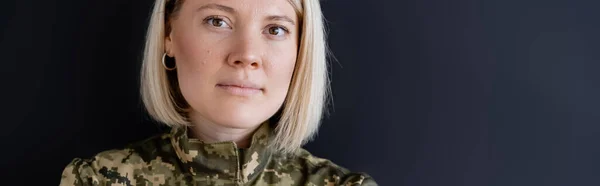 Porträt einer blonden Militärfrau, die isoliert auf schwarz in die Kamera blickt, Banner — Stockfoto