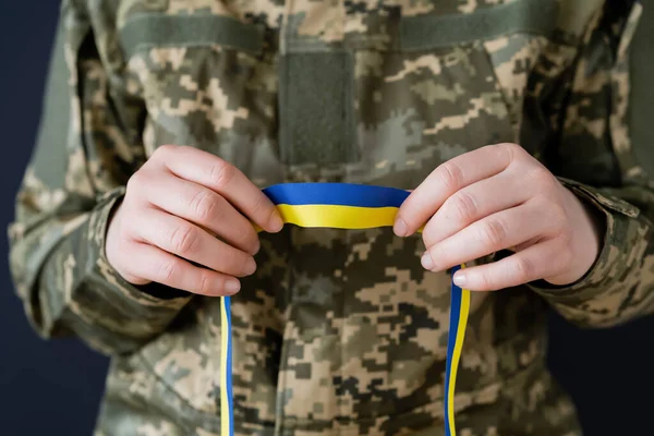 Partial view of woman in military uniform holding blue and yellow ribbon isolated on black — Stock Photo