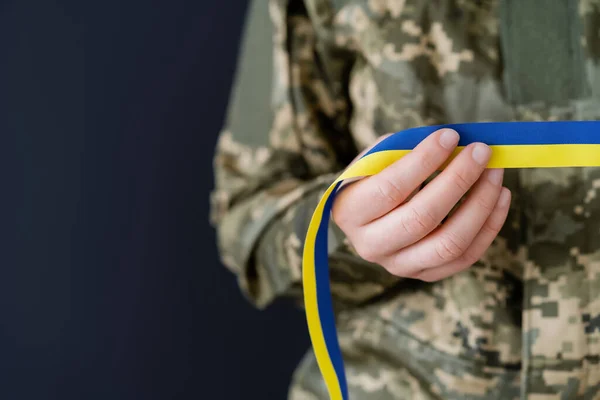 Partial view of woman in military uniform holding blue and yellow ribbon isolated on black — Stock Photo