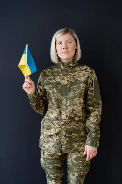 Vista frontal de la mujer militar con bandera ucraniana mirando a la cámara aislada en negro - foto de stock