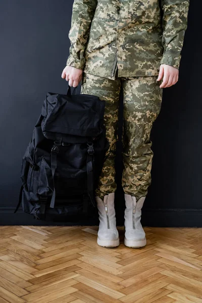 Vue recadrée de la femme militaire avec sac à dos noir près du mur sombre — Photo de stock