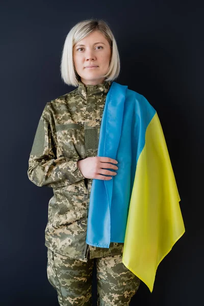 Donna militare bionda con bandiera ucraina guardando la fotocamera isolata sul nero — Foto stock