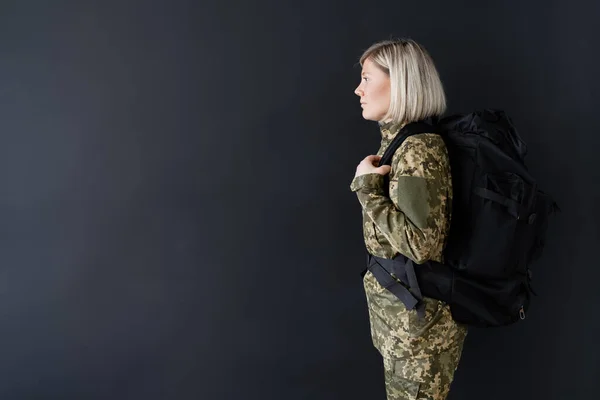 Vista lateral de mulher militar loira com mochila isolada em preto — Fotografia de Stock