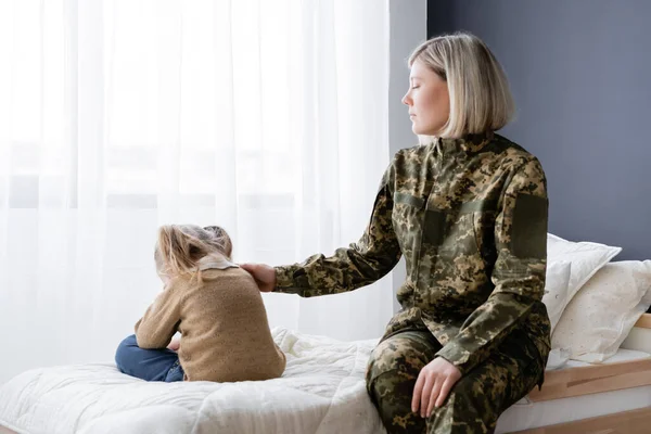 Military woman touching upset daughter sitting on bed at home — Stock Photo