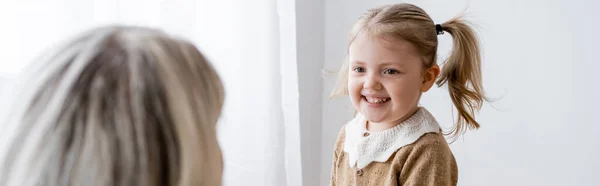 Fröhliches Mädchen, das Mama auf verschwommenem Vordergrund zu Hause ansieht, Banner — Stockfoto