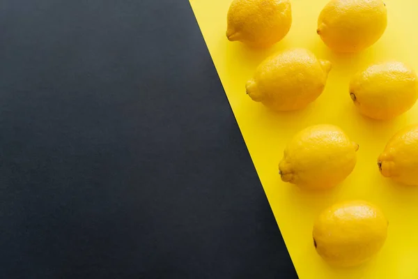 Flat lay with fresh lemons on black and yellow background with copy space — стоковое фото