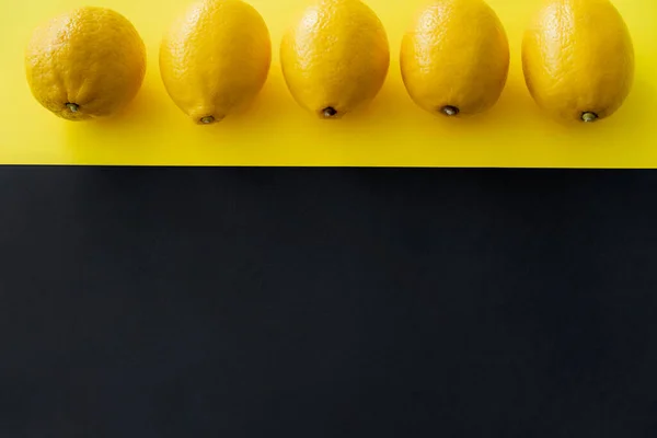 Vue du dessus de la rangée de citrons frais sur fond noir et jaune — Photo de stock