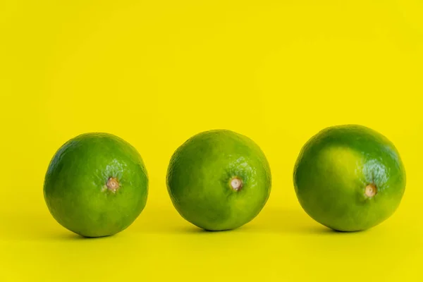Ripe limes on yellow surface with copy space — Stock Photo