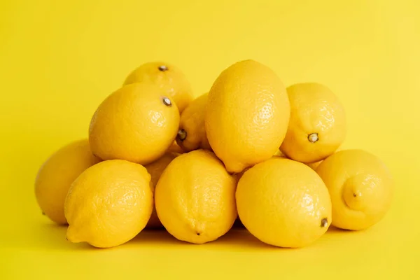 Heap of fresh lemons on yellow surface — Photo de stock