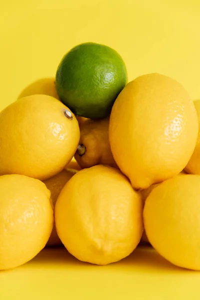 Close up view of green lime on lemons on yellow surface — Stockfoto