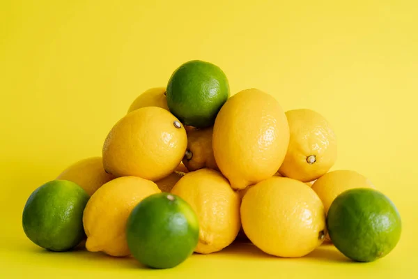 Heap of limes and lemons on yellow surface — Stockfoto