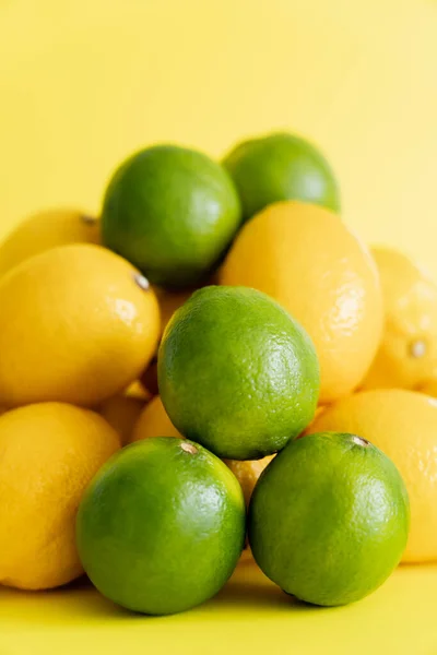 Close up view of organic limes near blurred lemons on yellow surface — стоковое фото