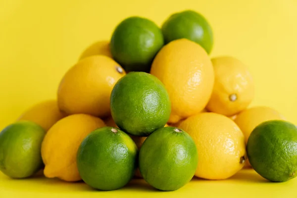 Сочные лаймы возле кучи размытых лимонов на желтой поверхности — стоковое фото