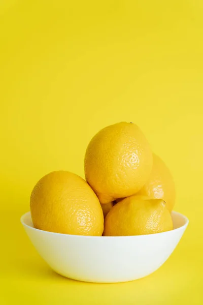 Organic lemons in bowl on yellow surface — стоковое фото