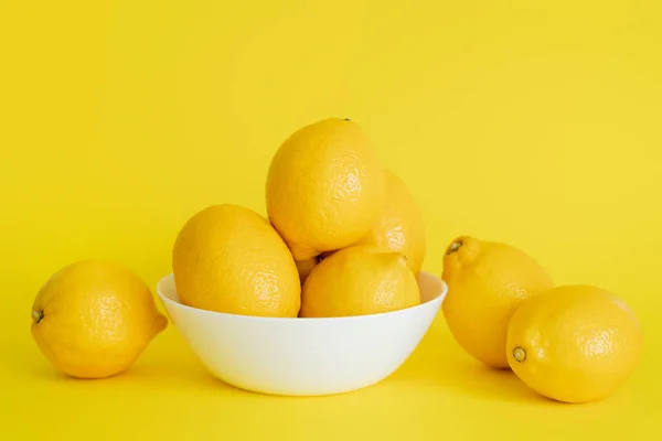 Fresh lemons in bowl and on yellow surface — Fotografia de Stock