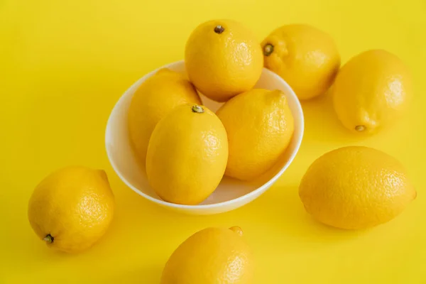 Vista en ángulo alto de limones maduros en recipiente sobre superficie amarilla - foto de stock