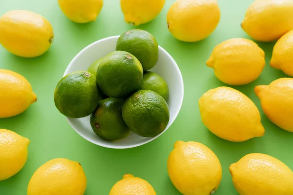 Top view of limes in bowl near lemons on green background — Photo de stock