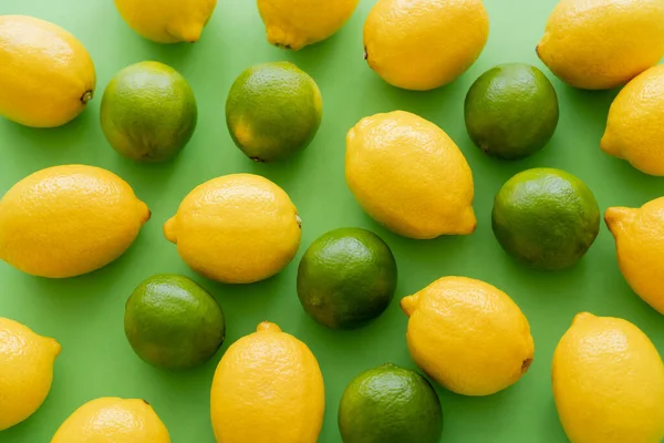 Colocación plana de limones y limas sobre fondo verde - foto de stock