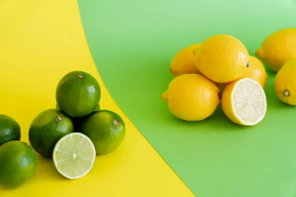 Limes near blurred lemons on green and yellow background — стоковое фото