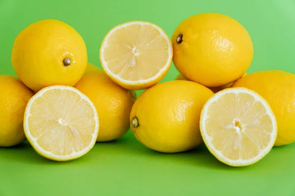 Halves and whole lemons on green background — Stock Photo