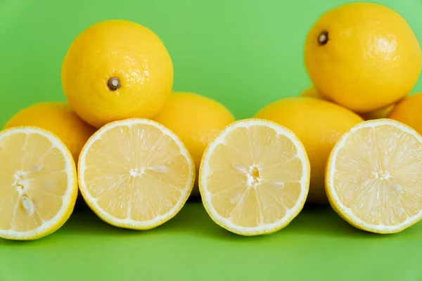 Mitades brillantes y limones enteros sobre fondo verde - foto de stock