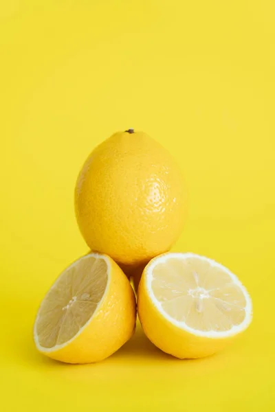 Vista de cerca de los limones cortados y enteros sobre fondo amarillo - foto de stock