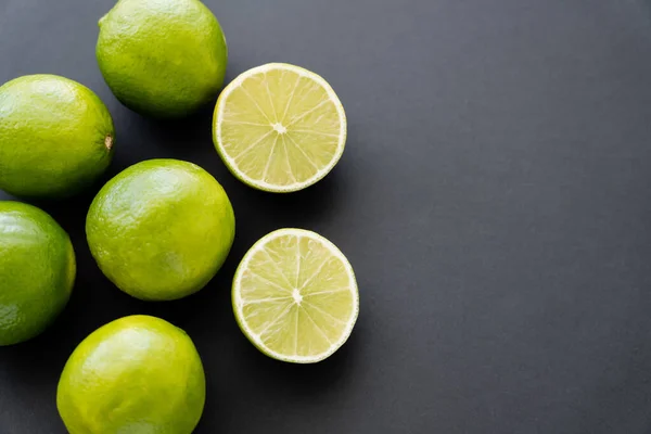 Top view of whole and cut limes on black background with copy space — стоковое фото