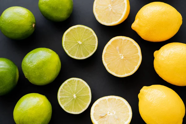 Flat lay of whole and cut lemons and limes on black background — Fotografia de Stock