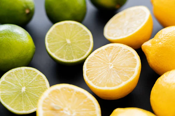 Close up view of bright lemons and limes near blurred fruits on black background — Photo de stock