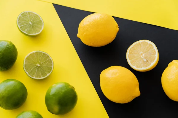 Vue de dessus des citrons et citrons frais sur fond noir et jaune — Photo de stock