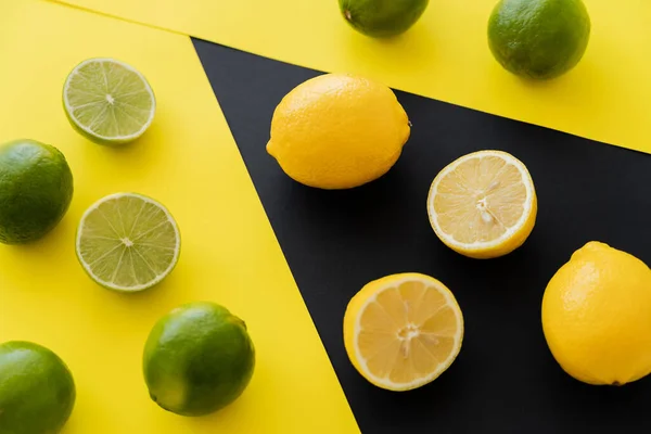 Top view of fresh lemons on black and limes on yellow background — Fotografia de Stock