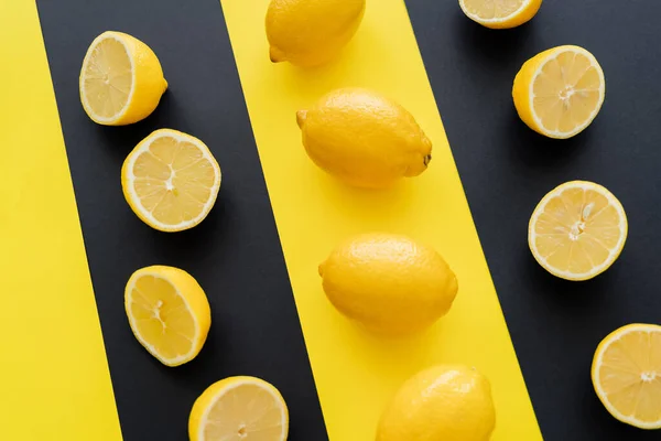 Acostado plano con mitades y limones enteros sobre fondo negro y amarillo - foto de stock