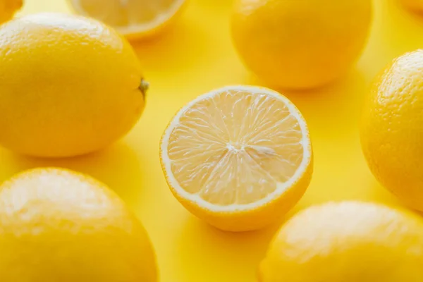 Close up view of cut and blurred whole lemons on yellow surface - foto de stock