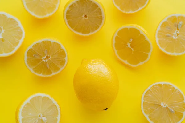 Vista superior de limones enteros y mitades de limones orgánicos en superficie amarilla - foto de stock