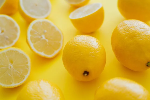 Vista de cerca de limones frescos cerca de mitades borrosas en la superficie amarilla - foto de stock