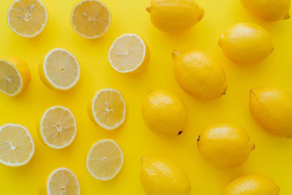 Acostado plano con mitades y limones enteros sobre superficie amarilla - foto de stock