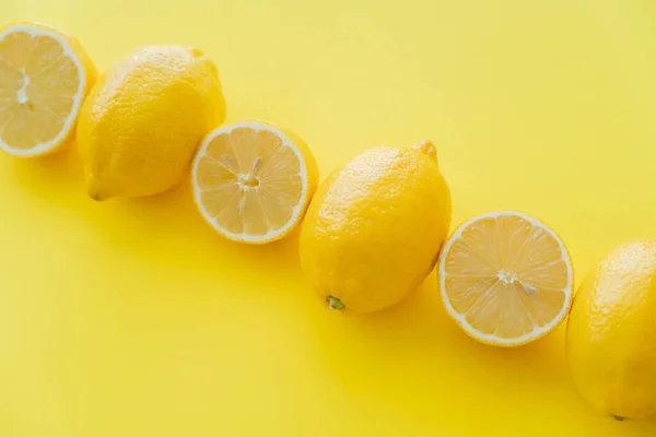 Poser à plat avec des moitiés et des citrons entiers sur la surface jaune — Photo de stock