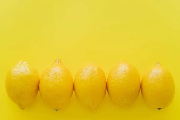 Top view of row of lemons on yellow surface with copy space — Stock Photo