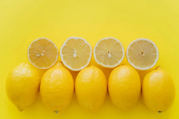 Vista superior de filas de limones enteros y cortados sobre superficie amarilla - foto de stock