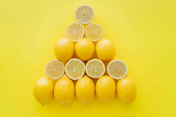 Colocação plana com limões inteiros e cortados em forma de triângulo na superfície amarela — Fotografia de Stock