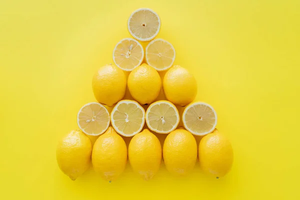 Colocación plana con limones enteros y cortados en forma de triángulo sobre superficie amarilla — Stock Photo