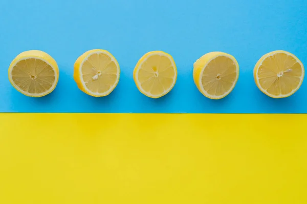 Vista superior de mitades maduras de limones sobre fondo azul y amarillo - foto de stock