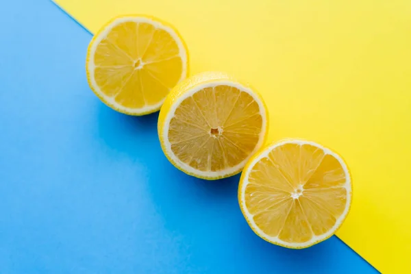 Vista superior de limones cortados sobre fondo azul y amarillo - foto de stock