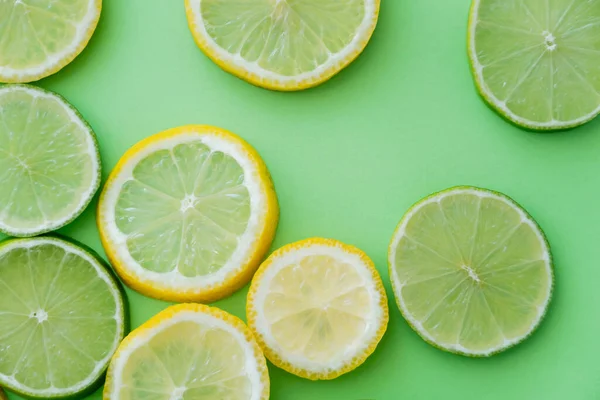 Vue du dessus de tranches de citrons et de limes sur fond vert — Photo de stock